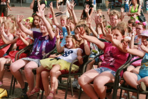 Tłum dzieci siedzący na krzesłach z wyciągniętymi palcami do góry