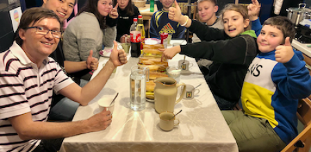 grupa młodzieży siedzi przy stole pokazując kciuki do góry